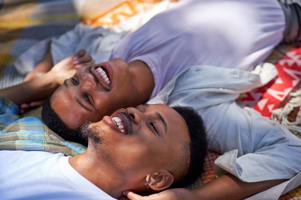 Two men who look alike laying on a blanket with their heads together