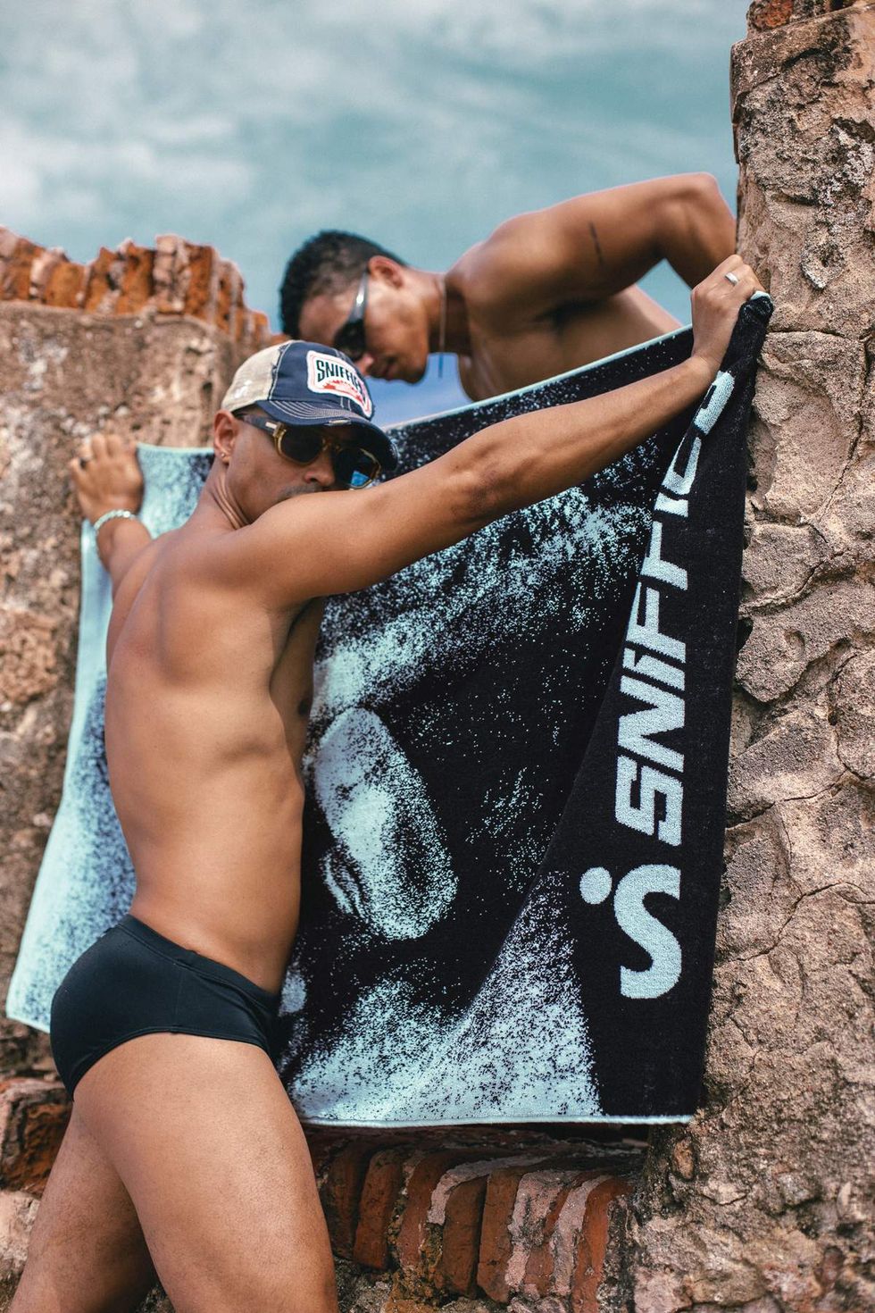 Two models pose with a Sniffies towel during the Sniffies Summer Swim Collection campaign in Puerto Rico