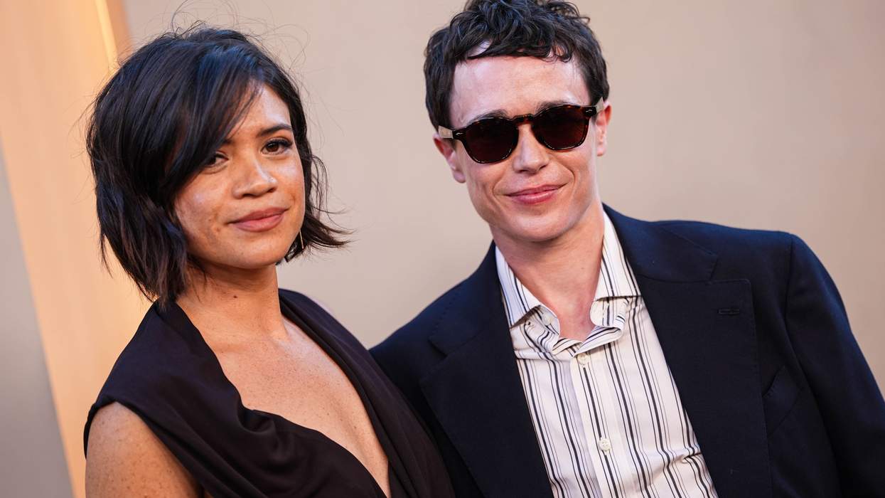 Two people posing together, one in sunglasses, both dressed formally.