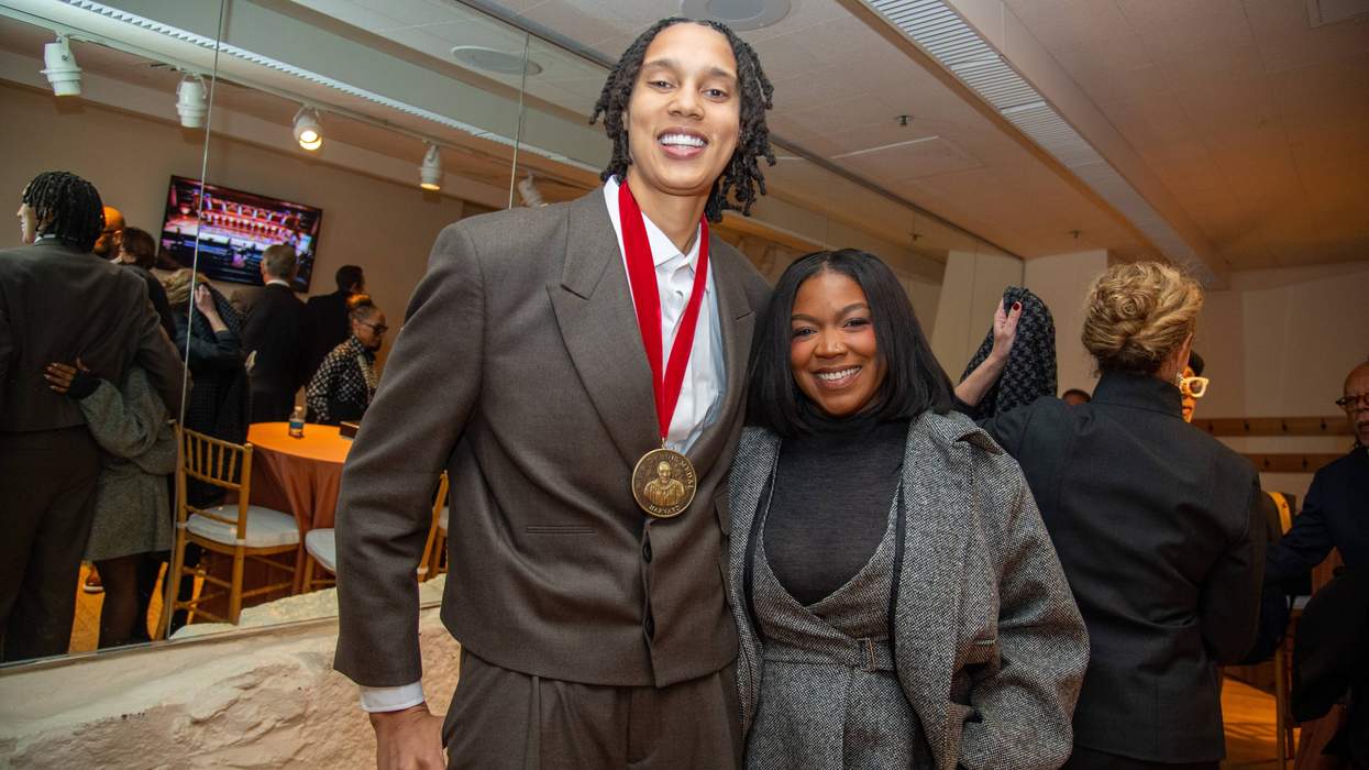 Two people smiling at an event, one wearing a medal, in a warmly lit room.