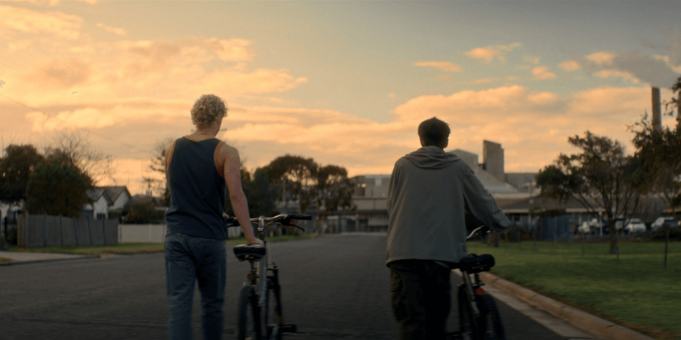 Two teenage boys walk their bicycles down a quiet suburban street at sunset in a scene from Leviticus