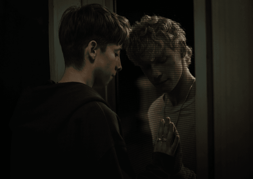 Two teenagers separated by a glass window in a scene from Leviticus