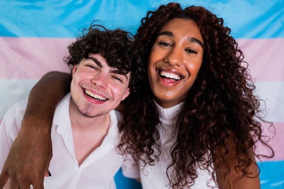 Two trans friends in front of the trans pride flag