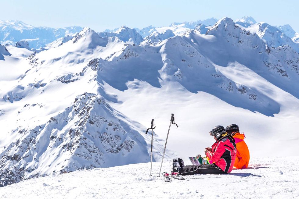 Two women in ski gear sitting in the snow.