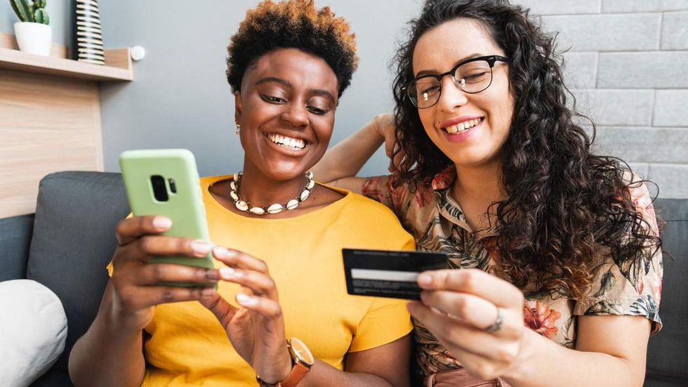 two women on a couch smile while online shopping