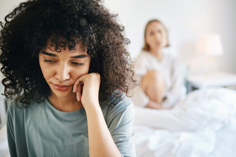 Two women sitting on a bed, one with her head on her chin
