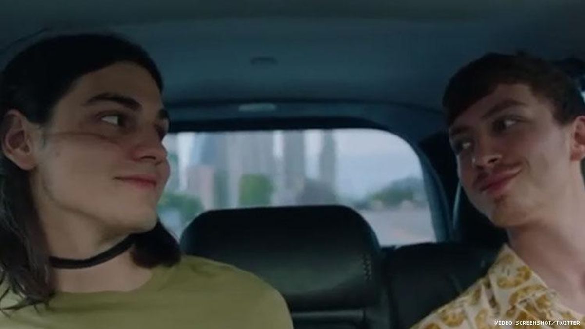 Two young gay boys sitting in the back of a car looking at one another.
