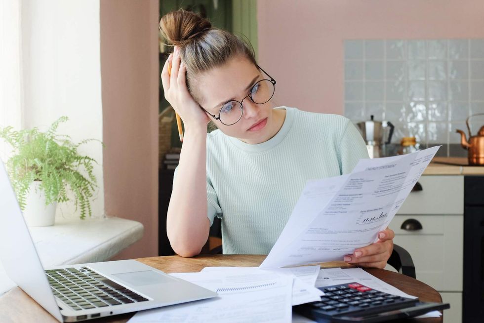 \u200bA woman looking at bills with a laptop and calculator in front of her.