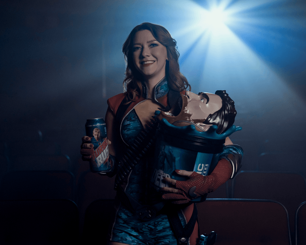 Valorie Curry as Firecracker holds a drink and a themed popcorn bucket in a movie theater