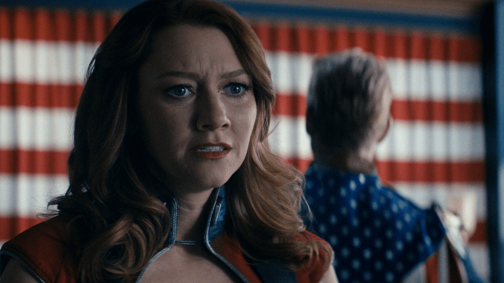 Valorie Curry as Firecracker looks distressed while Homelander, played by Antony Starr, stands blurred in the background in a scene from The Boys