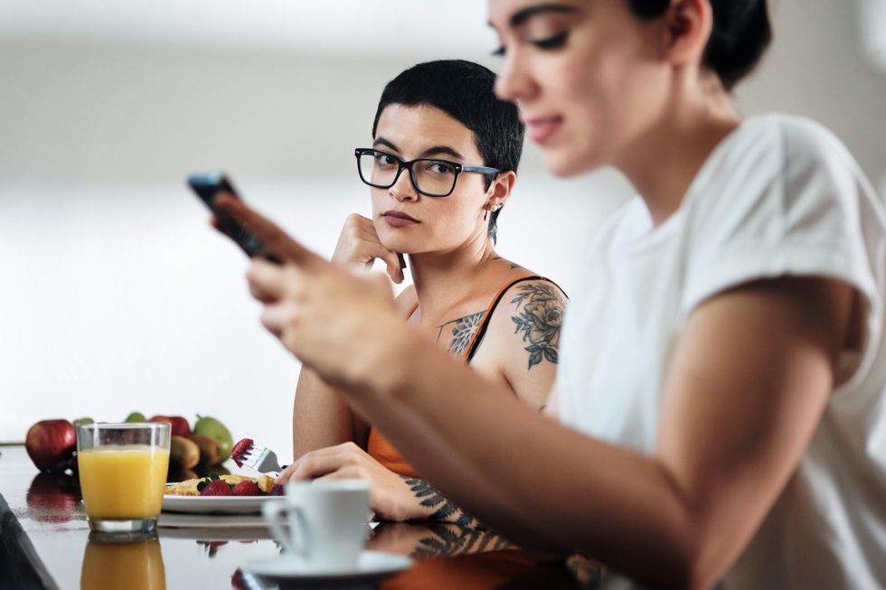 Woman looking at another woman who is on her cell phone