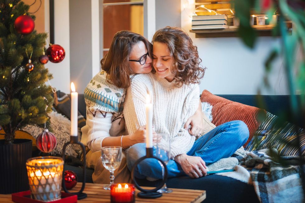 Young adult happy lesbian couple sitting on couch at home hugging and celebrating christmas and new year eve