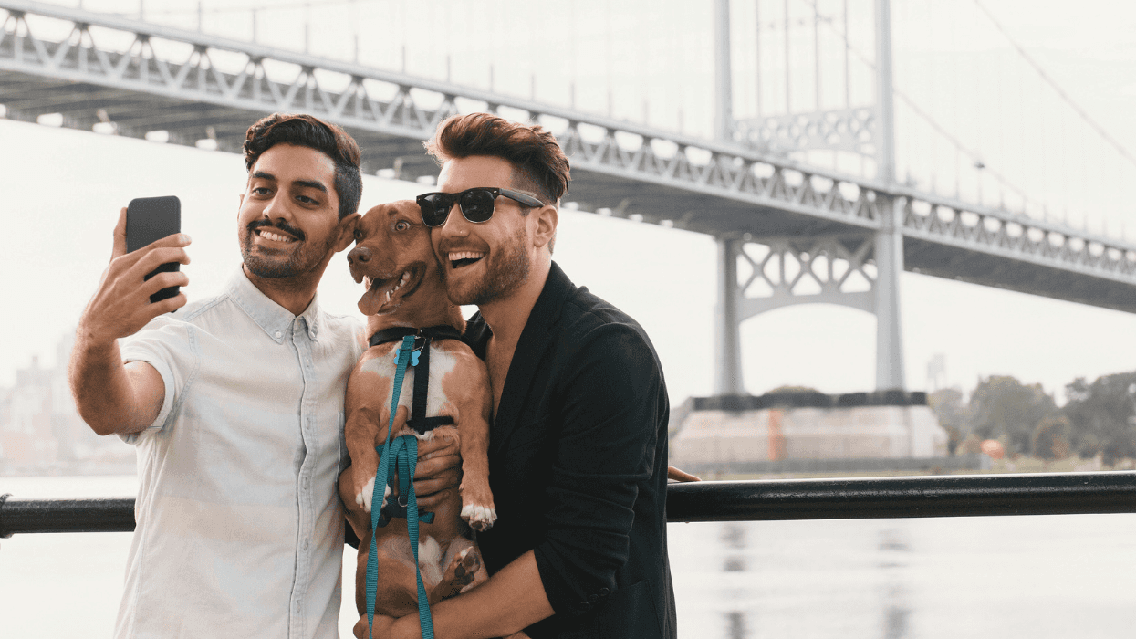 Young male couple on riverside taking smartphone selfie with dog, Astoria, New York, USA