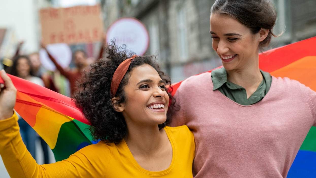 Young queer women hold LGBTQ+ Pride flag