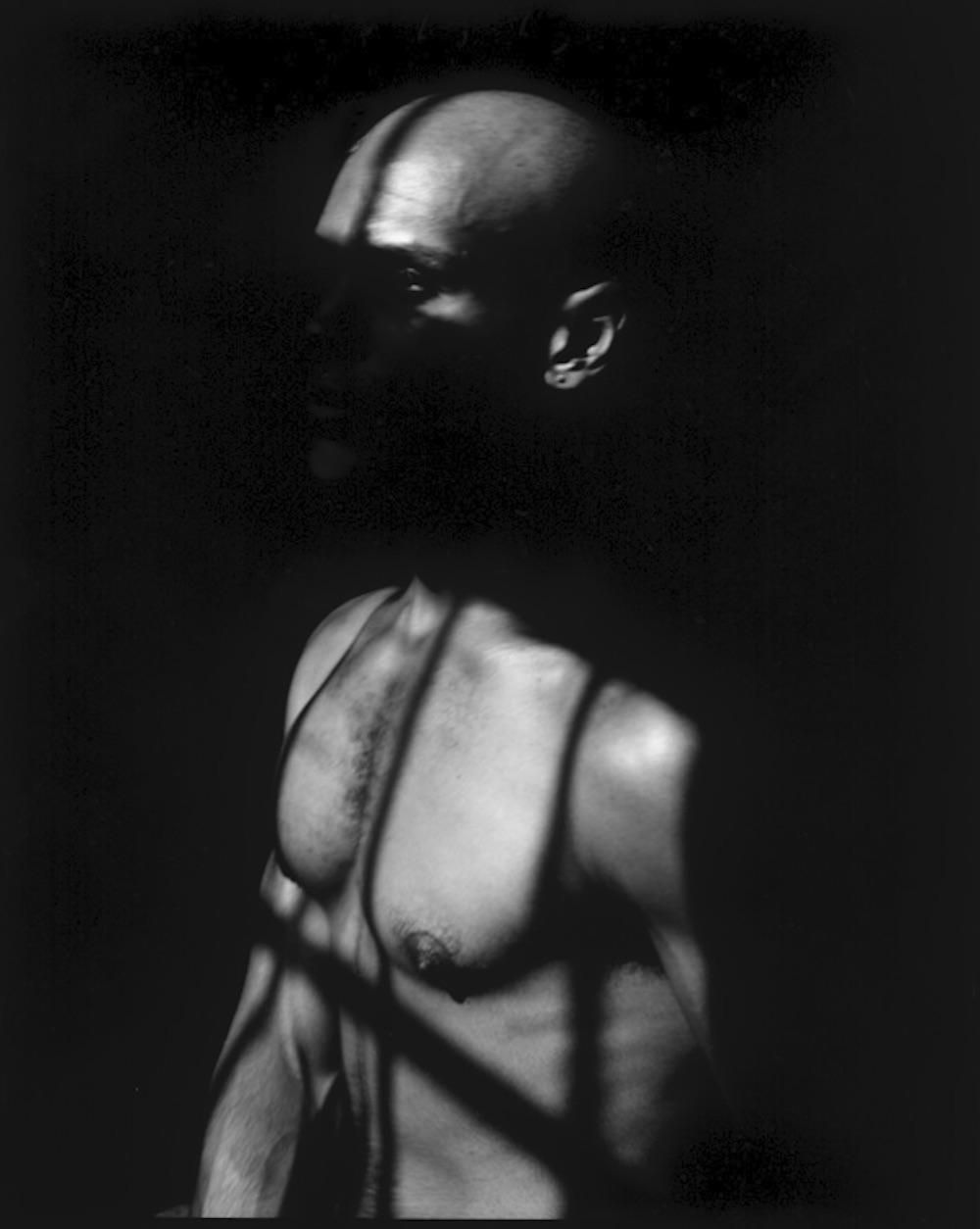 A shirtless man obscured in the shadows of a window.